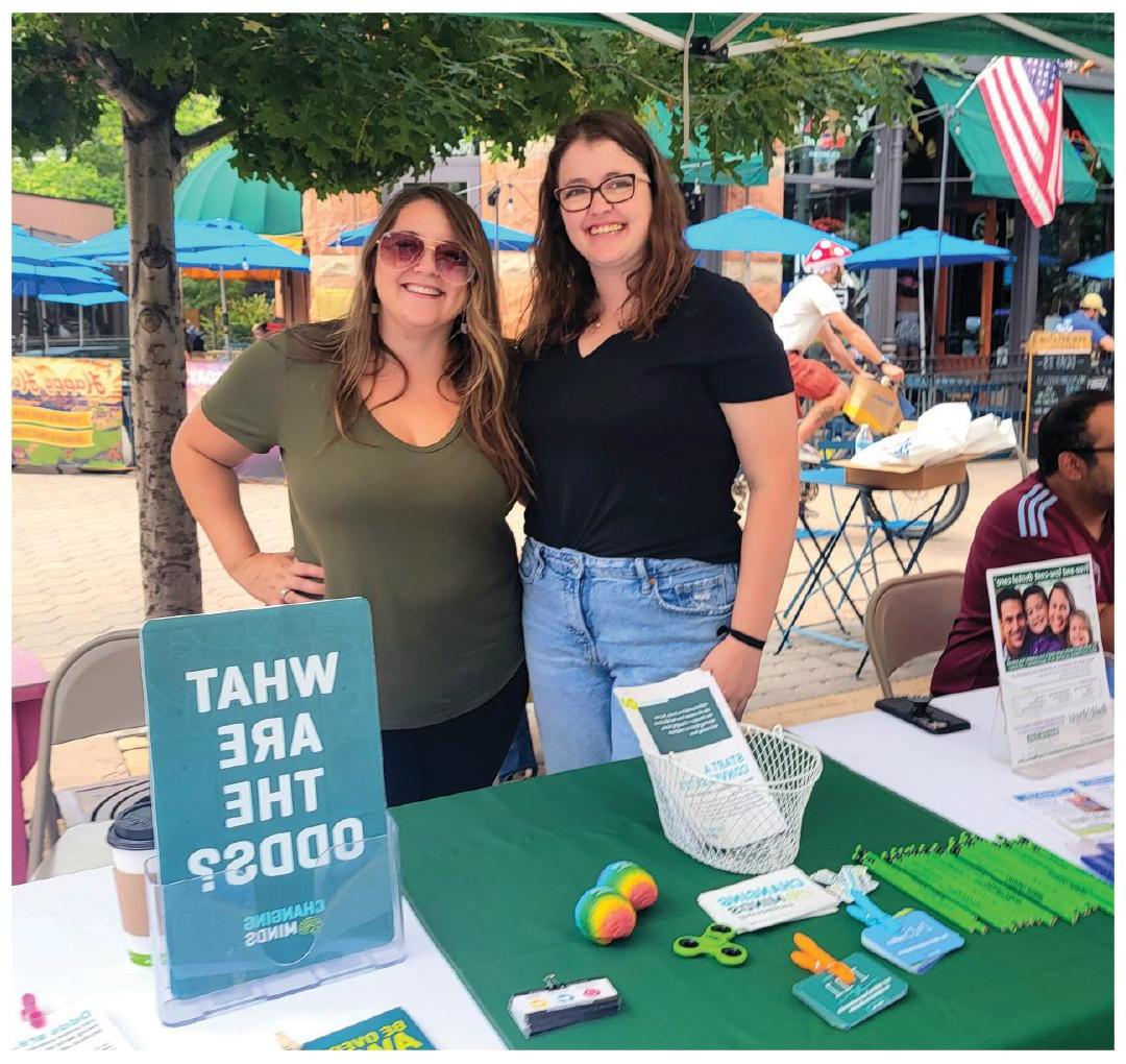 photo of two women standing at outdoor outreach table filled with Health District information to hand out